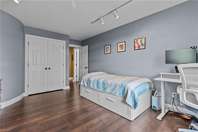 bedroom with track lighting, a closet, and dark hardwood / wood-style floors