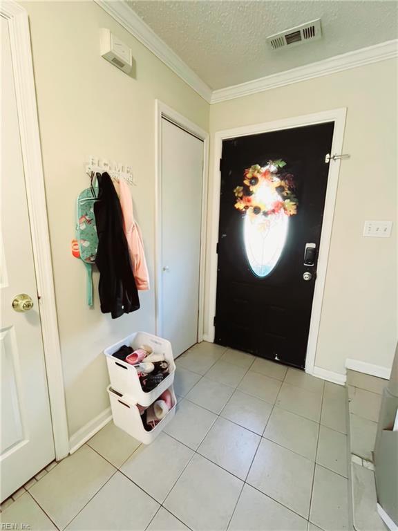 foyer featuring a textured ceiling, crown molding, and light tile patterned flooring