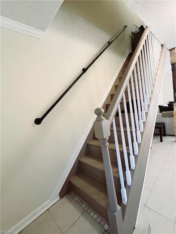 stairs with a textured ceiling, tile patterned floors, and crown molding