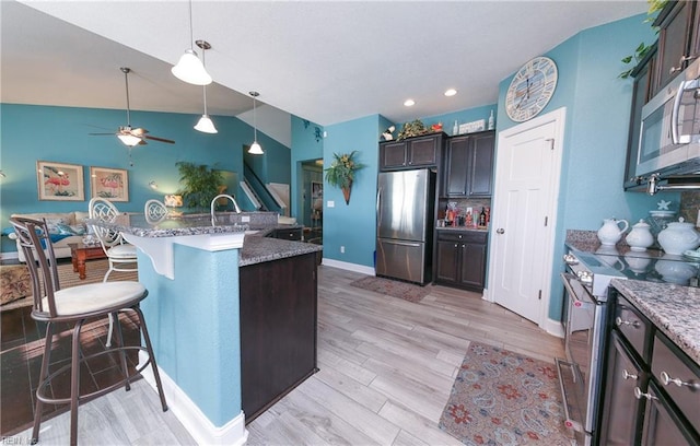 kitchen with ceiling fan, light stone countertops, a breakfast bar area, light wood-style flooring, and stainless steel appliances