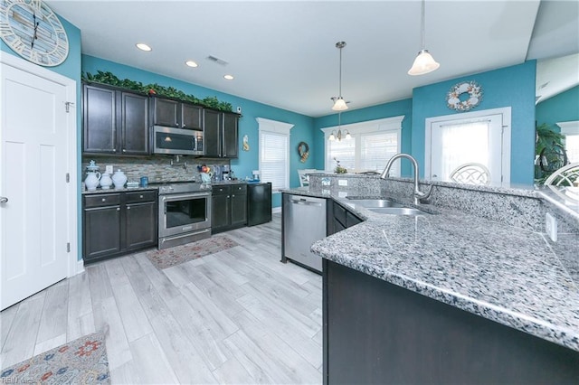 kitchen with sink, tasteful backsplash, light hardwood / wood-style flooring, pendant lighting, and appliances with stainless steel finishes