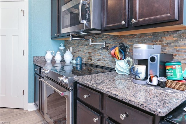 kitchen featuring backsplash, stainless steel appliances, light wood-style floors, light stone countertops, and dark brown cabinets