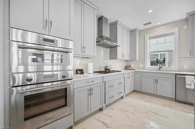 kitchen with decorative backsplash, wall chimney range hood, sink, and appliances with stainless steel finishes