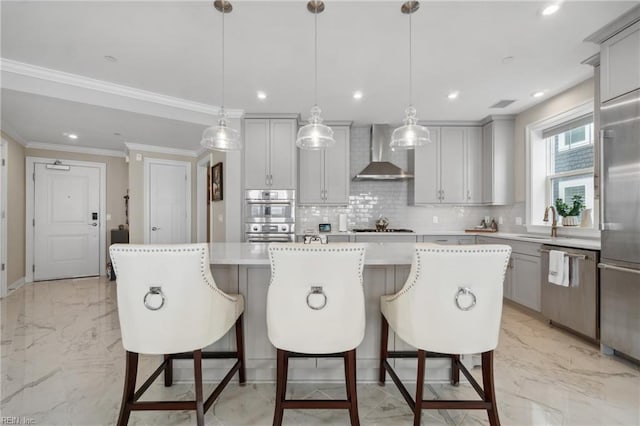 kitchen with appliances with stainless steel finishes, a center island, hanging light fixtures, and wall chimney range hood