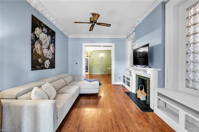 living room with hardwood / wood-style floors, crown molding, ceiling fan, built in features, and a fireplace