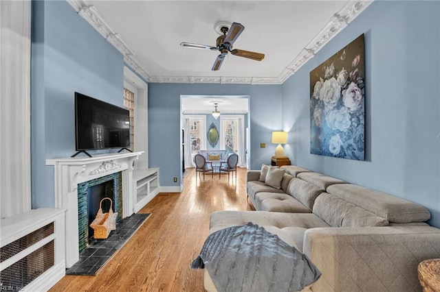 living room featuring a tile fireplace, hardwood / wood-style flooring, ceiling fan, and crown molding