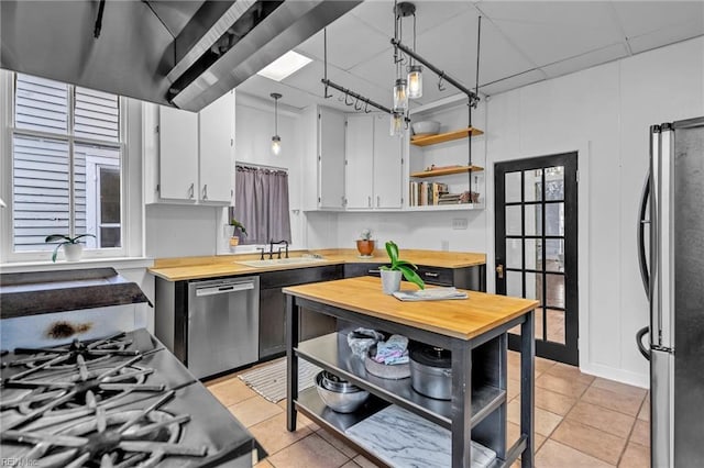 kitchen with appliances with stainless steel finishes, sink, white cabinetry, hanging light fixtures, and light tile patterned flooring