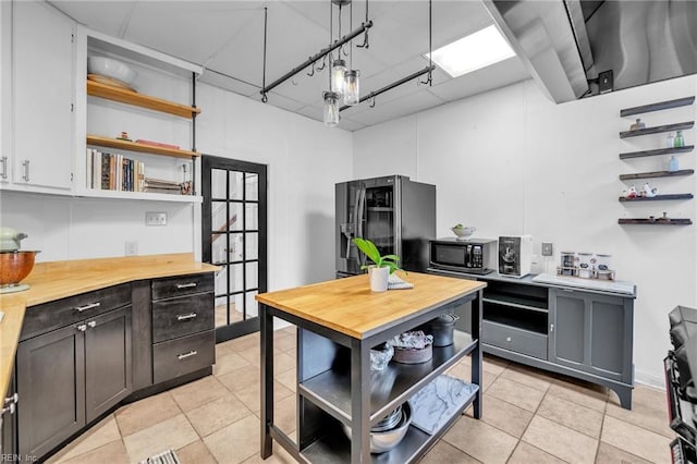 kitchen with wood counters, stainless steel fridge, light tile patterned flooring, and hanging light fixtures