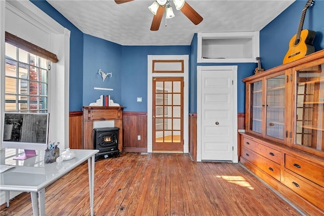 office space featuring hardwood / wood-style floors, a wood stove, ceiling fan, and wooden walls