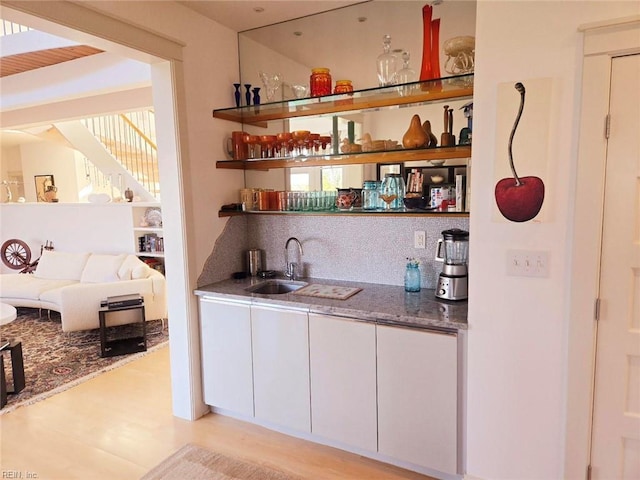 bar featuring backsplash, sink, dark stone countertops, light wood-type flooring, and white cabinetry