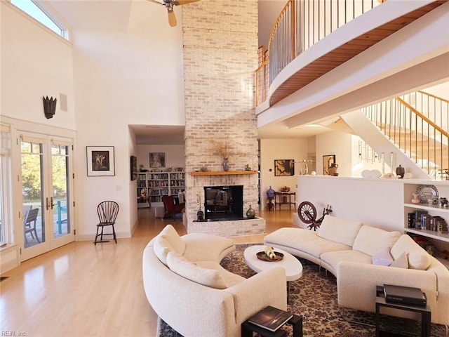 living room with a brick fireplace, light wood-type flooring, a high ceiling, and french doors