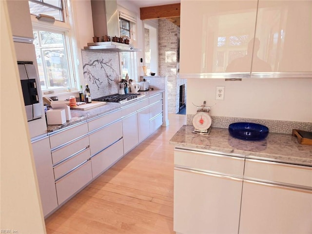 kitchen with ventilation hood, stainless steel gas stovetop, white cabinets, and light stone counters