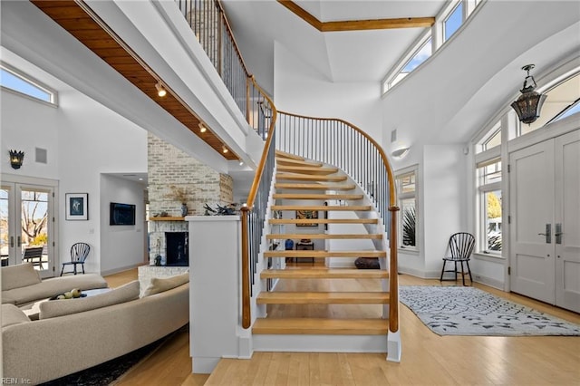 foyer featuring a high ceiling, light wood-type flooring, a brick fireplace, and beam ceiling