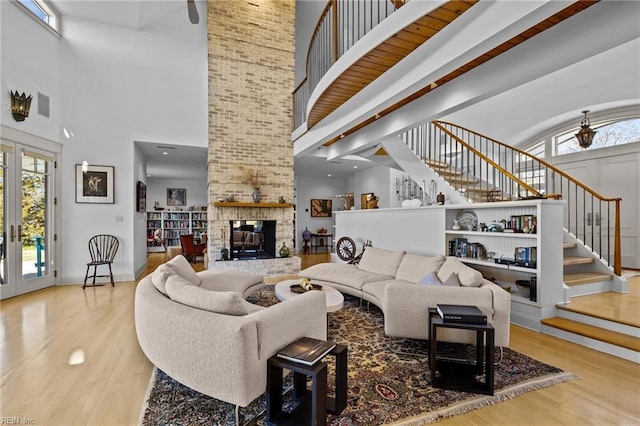 living room with a high ceiling, light hardwood / wood-style floors, a brick fireplace, and french doors