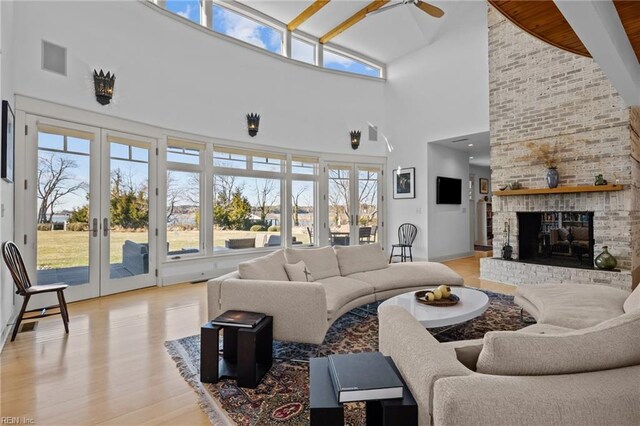 living room featuring french doors, a brick fireplace, ceiling fan, light hardwood / wood-style flooring, and high vaulted ceiling