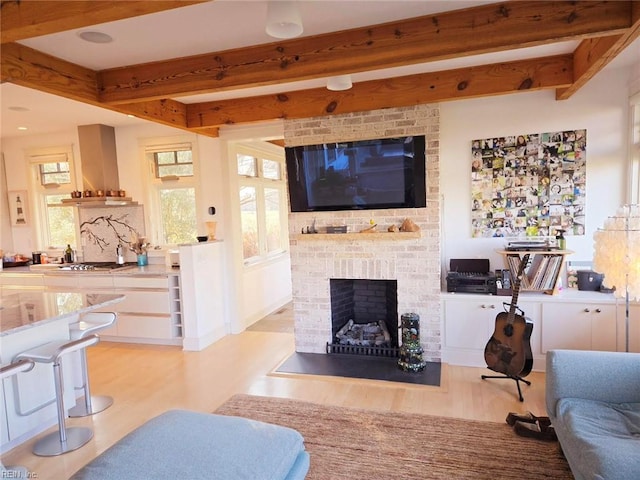 living room featuring a brick fireplace, beamed ceiling, and light wood-type flooring