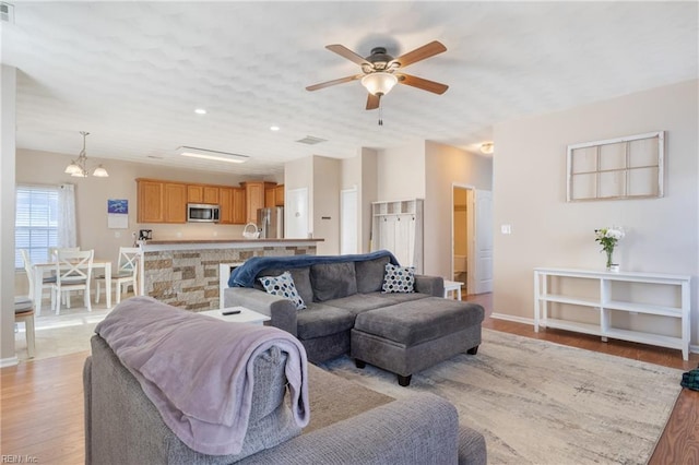 living room with ceiling fan with notable chandelier and light wood-type flooring