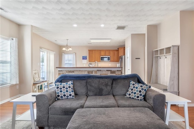 living room with sink, light hardwood / wood-style flooring, and an inviting chandelier