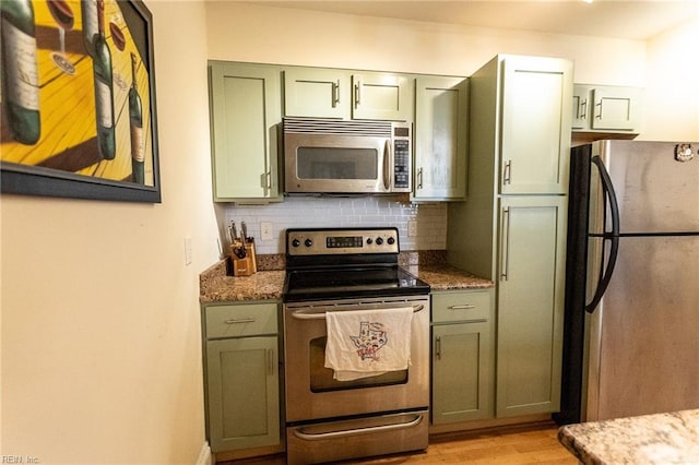 kitchen with light wood-type flooring, tasteful backsplash, dark stone counters, stainless steel appliances, and green cabinetry