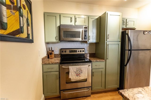 kitchen with decorative backsplash, light wood-type flooring, dark stone counters, stainless steel appliances, and green cabinetry