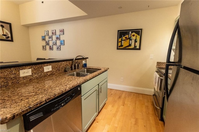 kitchen featuring dark stone countertops, sink, stainless steel appliances, and light wood-type flooring