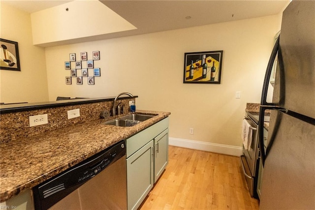 kitchen with light wood-type flooring, stainless steel appliances, dark stone countertops, and sink