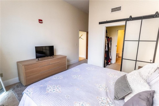 carpeted bedroom featuring ensuite bath, a barn door, a towering ceiling, and a closet