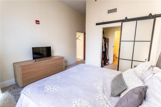 bedroom with a barn door, a spacious closet, connected bathroom, light colored carpet, and a closet