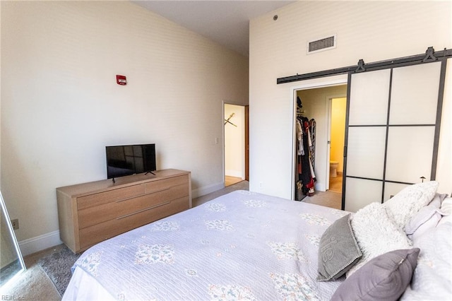 bedroom featuring light carpet, a barn door, high vaulted ceiling, connected bathroom, and a closet