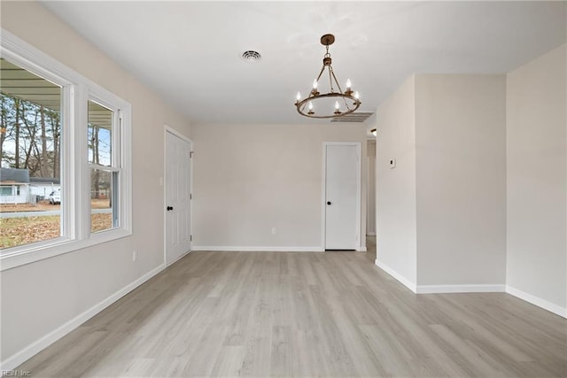 empty room with light hardwood / wood-style floors and an inviting chandelier