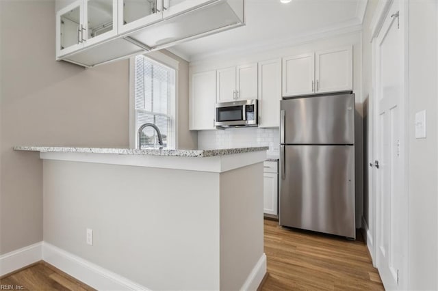 kitchen with white cabinetry, kitchen peninsula, decorative backsplash, appliances with stainless steel finishes, and light wood-type flooring