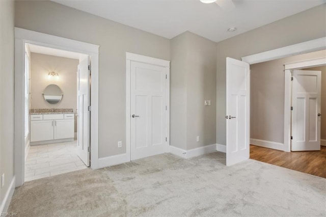 unfurnished bedroom with light carpet, a closet, ensuite bath, and ceiling fan