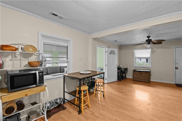 kitchen with ceiling fan, light hardwood / wood-style floors, ornamental molding, and a textured ceiling