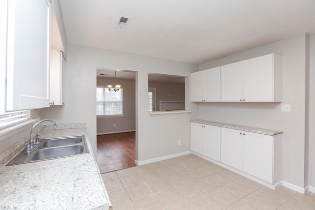 kitchen with light tile patterned floors, white cabinetry, a notable chandelier, and sink