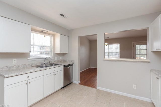 kitchen featuring white cabinets, sink, stainless steel dishwasher, light tile patterned floors, and light stone counters