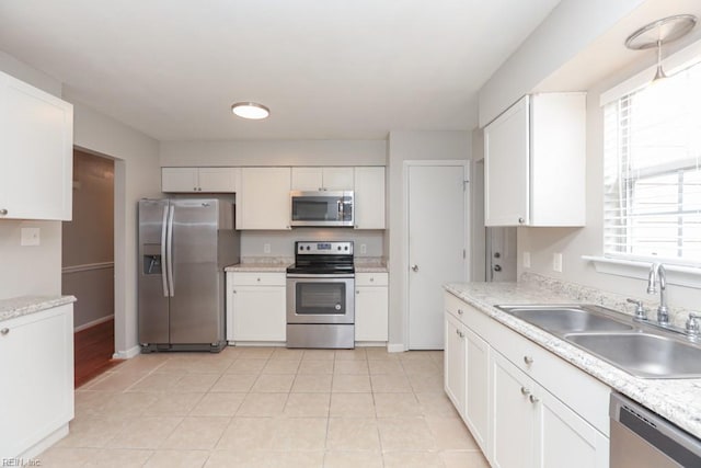 kitchen with appliances with stainless steel finishes, light stone counters, sink, light tile patterned floors, and white cabinets