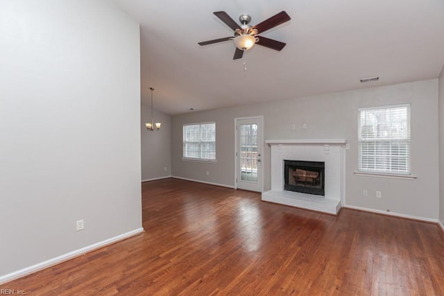 unfurnished living room with ceiling fan with notable chandelier, dark hardwood / wood-style flooring, lofted ceiling, and a brick fireplace