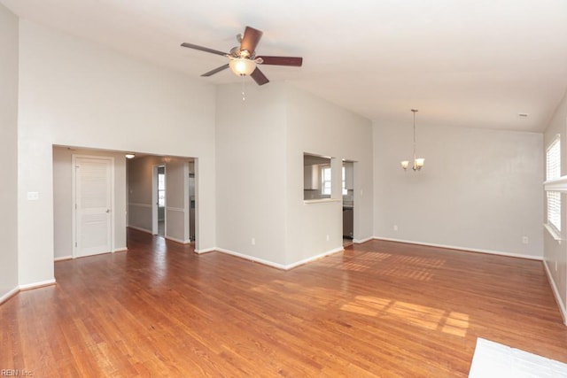 unfurnished living room featuring plenty of natural light, high vaulted ceiling, wood-type flooring, and ceiling fan with notable chandelier