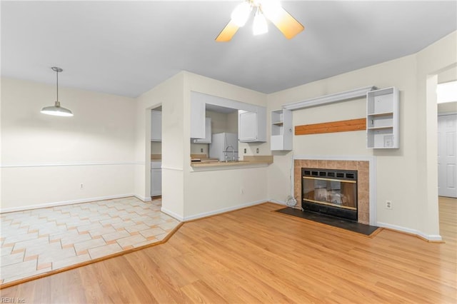 unfurnished living room featuring ceiling fan, a tiled fireplace, and light hardwood / wood-style flooring