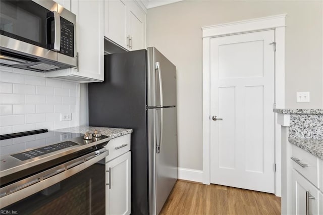 kitchen with light stone countertops, appliances with stainless steel finishes, backsplash, white cabinets, and light hardwood / wood-style floors