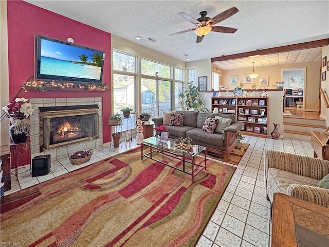 living room featuring tile patterned flooring, ceiling fan, a textured ceiling, and a tiled fireplace