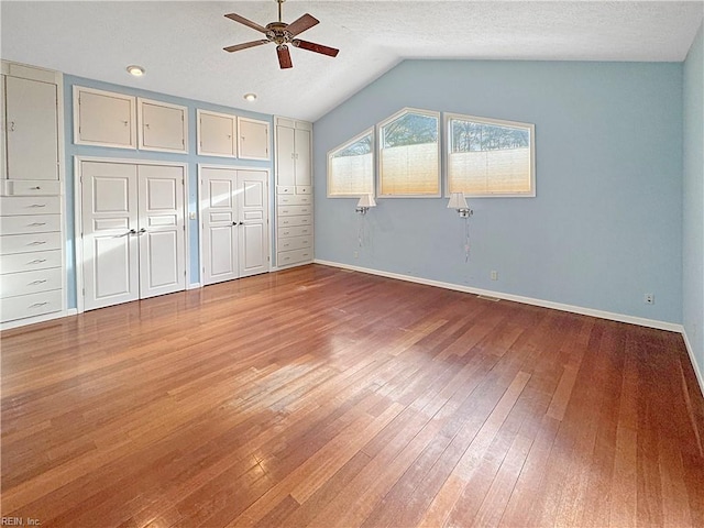 unfurnished bedroom featuring lofted ceiling, two closets, ceiling fan, a textured ceiling, and wood-type flooring