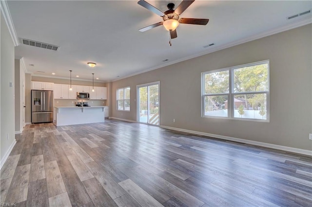 unfurnished living room featuring a healthy amount of sunlight, light wood-type flooring, ceiling fan, and crown molding