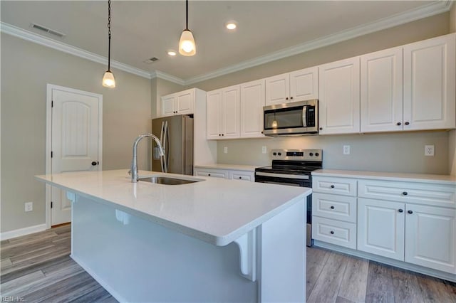 kitchen featuring a kitchen island with sink, white cabinets, light wood-type flooring, decorative light fixtures, and stainless steel appliances