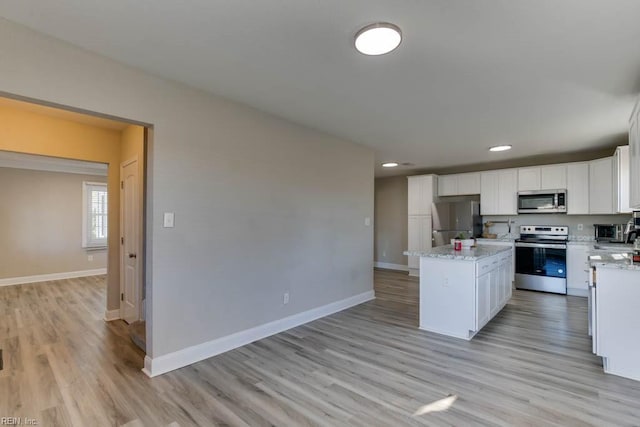 kitchen featuring white cabinets, appliances with stainless steel finishes, a center island, and light stone counters