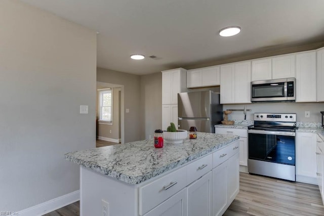 kitchen featuring a kitchen island, light stone counters, white cabinetry, and appliances with stainless steel finishes