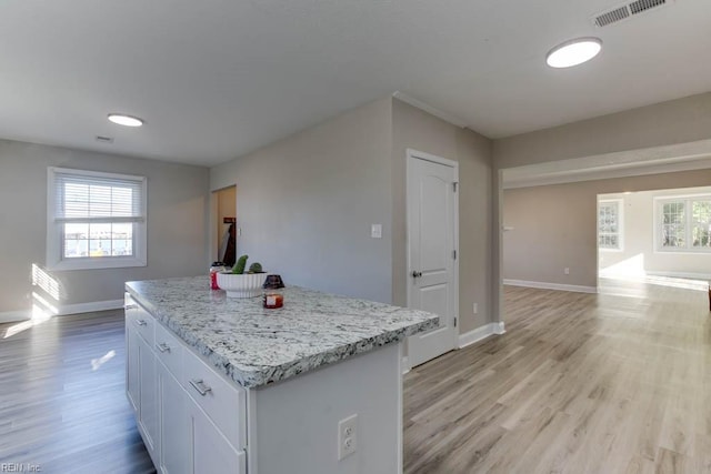 kitchen with light stone counters, white cabinets, light wood-type flooring, and a kitchen island