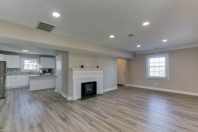 unfurnished living room with a fireplace, sink, ornamental molding, and light wood-type flooring