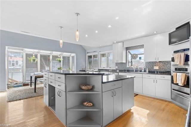 kitchen with backsplash, stainless steel double oven, a kitchen island, decorative light fixtures, and white cabinetry