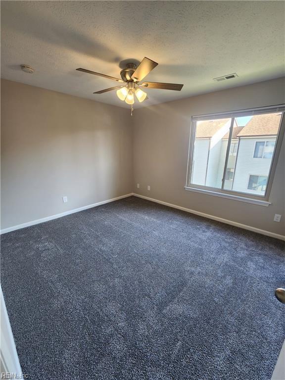 empty room featuring ceiling fan, dark carpet, and a textured ceiling